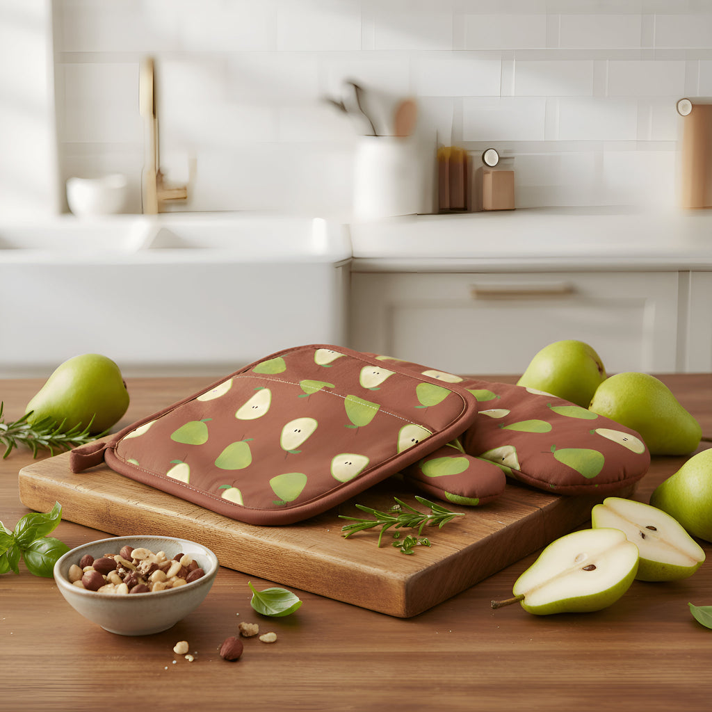 A set of brown oven mitt and pot holder with a green pear pattern, displayed on a wooden cutting board in a bright, modern kitchen setting with fresh pears and nuts from Hem And Tassel 