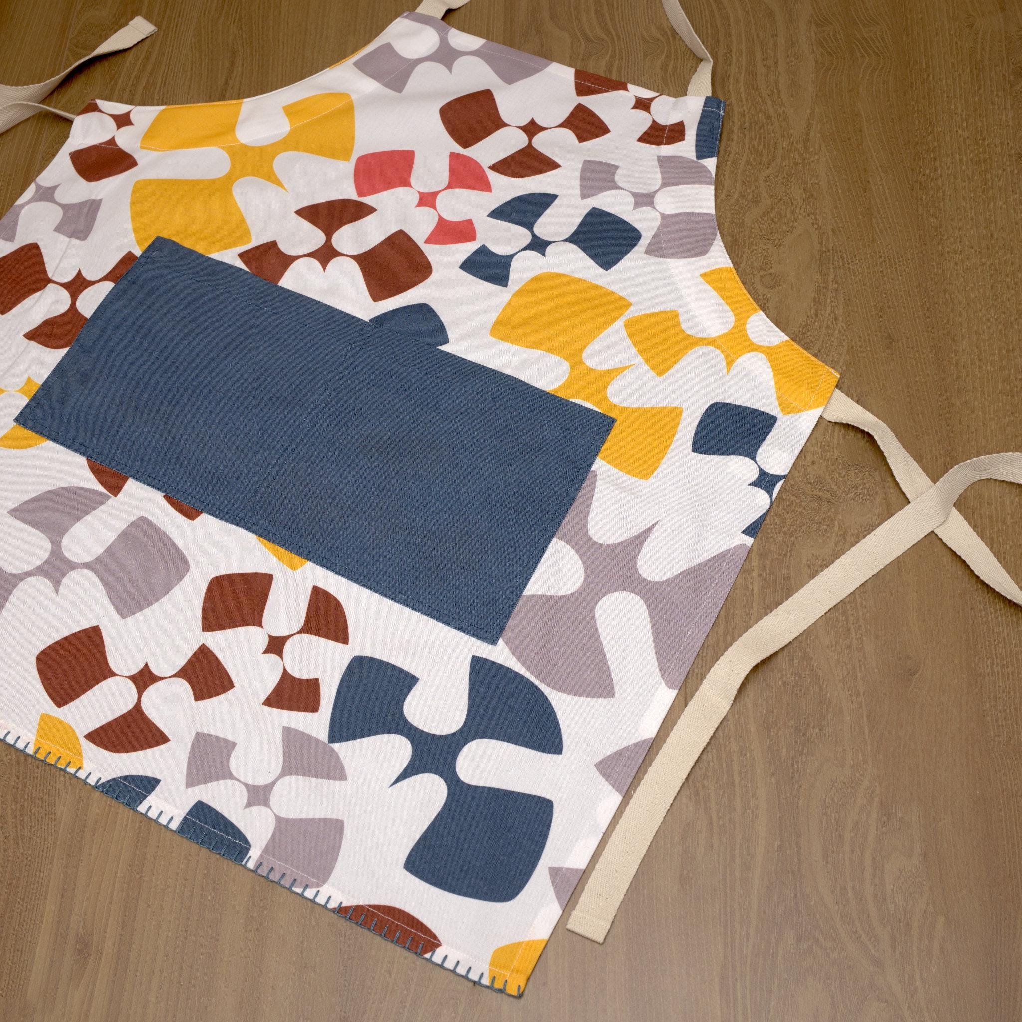 Colorful flock and flutter patterned cotton apron with a oil color pocket from Hem And Tassel, on a wood background