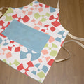  Colorful flock and flutter patterned cotton apron with a turquoise pocket from Hem And Tassel, on a wood background