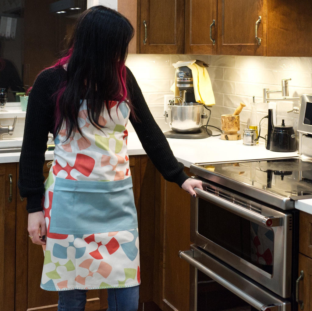 woman in kitchen wearing Colorful flock and flutter patterned cotton apron with a turquoise pocket from Hem And Tassel