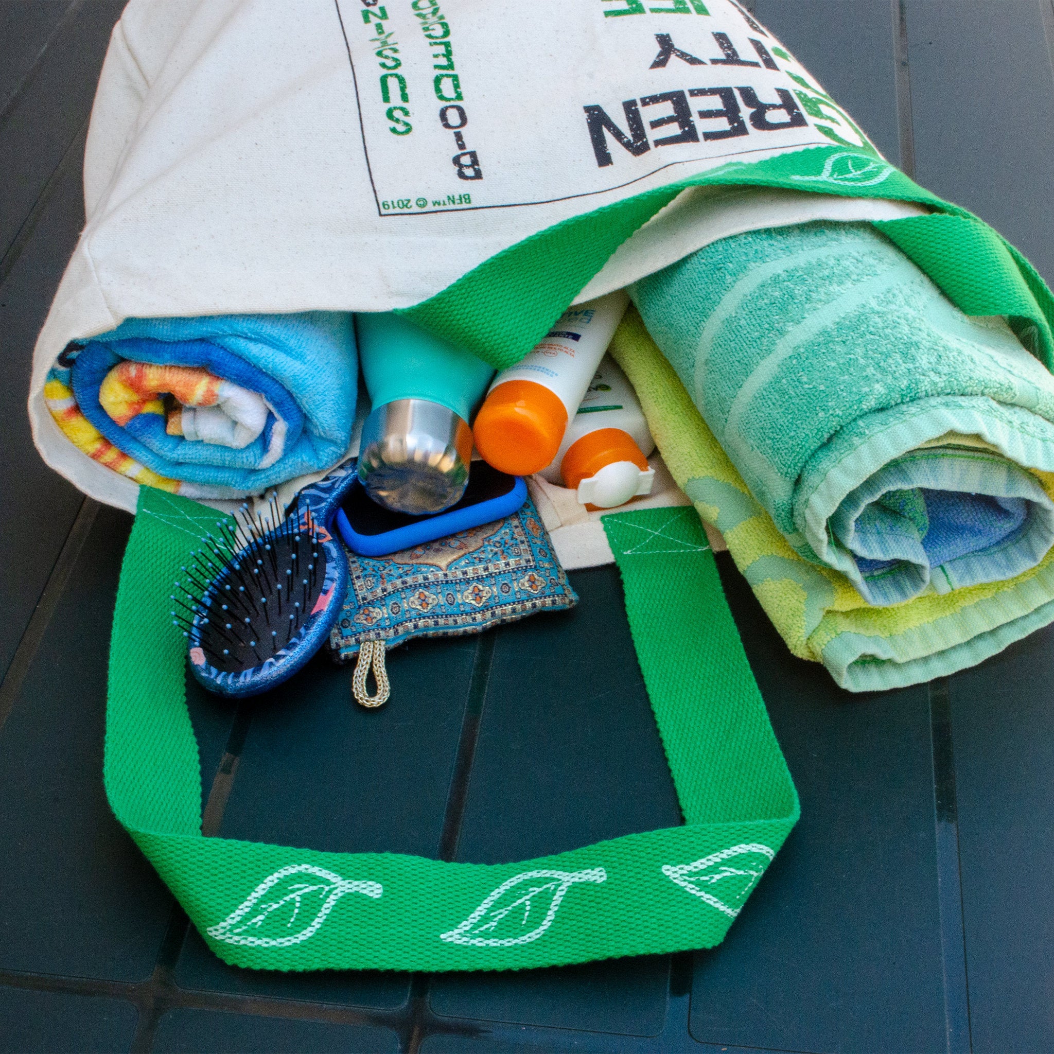 Green canvas tote bag with towels, bottles, and a brush on a black surface from Hem And Tassel 