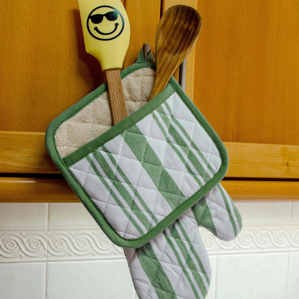 green decade classic oven mitt and quilted potholder with wooden spatula and spoon on a wooden cabinet. from hem and tassel