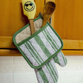 green decade classic oven mitt and quilted potholder with wooden spatula and spoon on a wooden cabinet. from hem and tassel