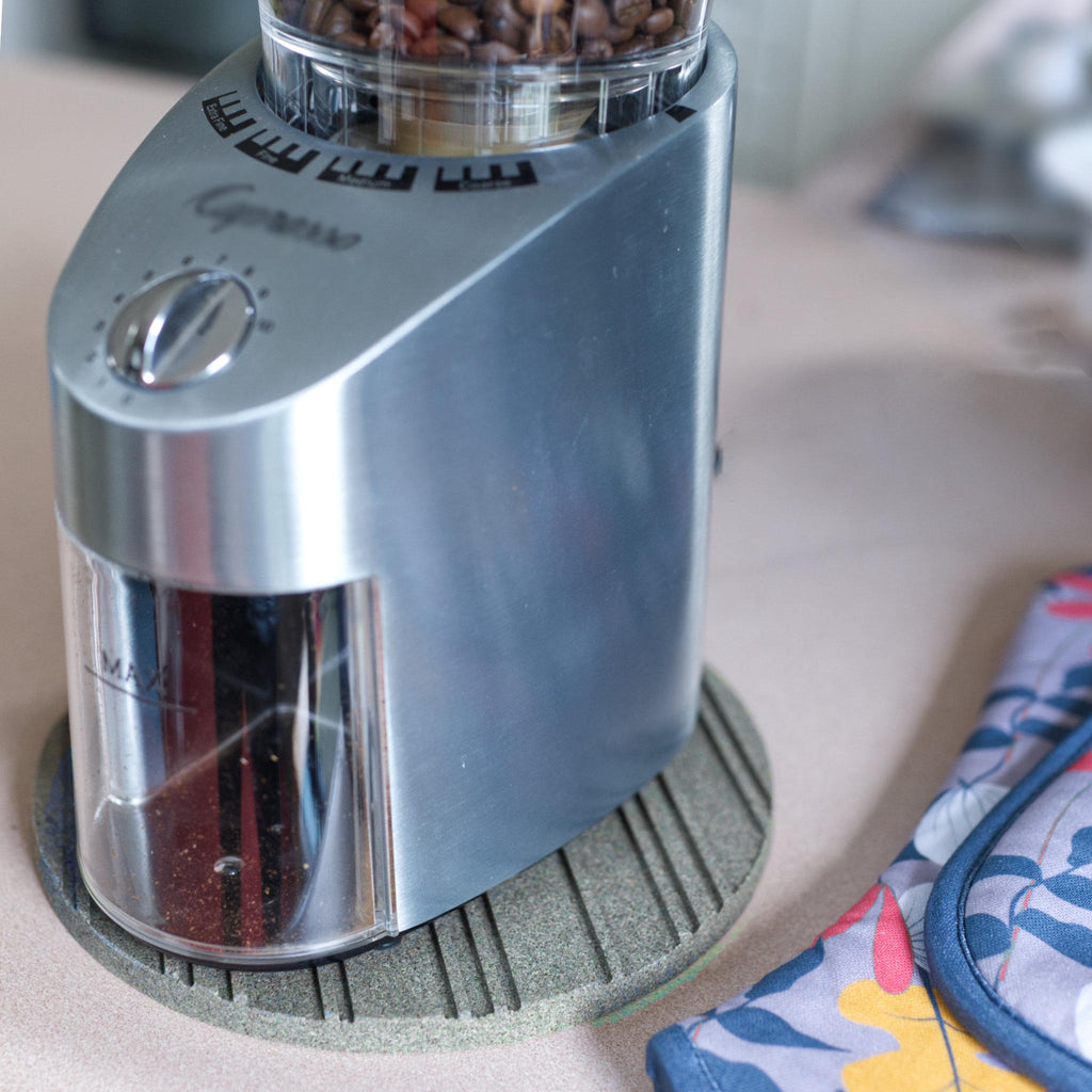 Silver coffee grinder on a countertop with a colorful kitchen towel in the background and heatsink cork trivet under the grinder from Hem And Tassel 