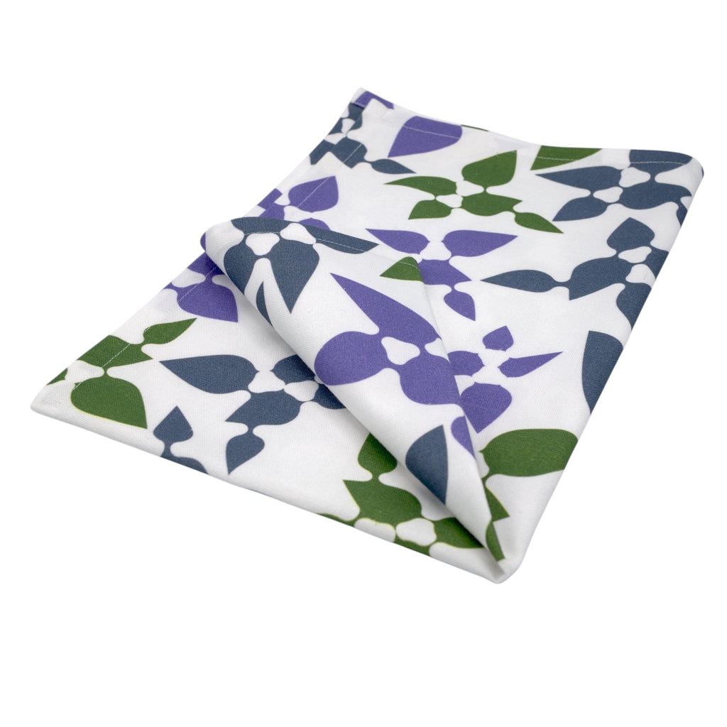 Hem And Tassel Celebration cotton kitchen towel with a white base and purple and green leaf confetti pattern.