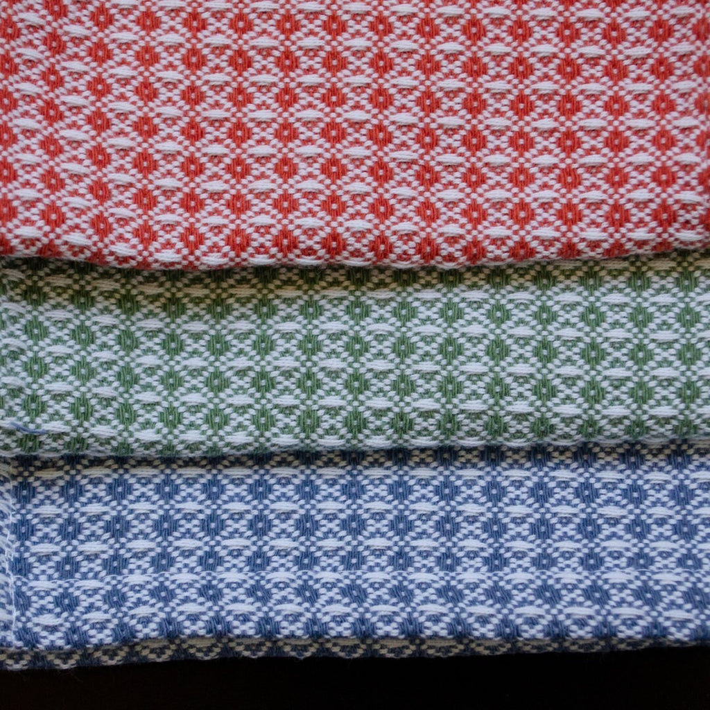 Hem And Tassel diamond waffle weave cotton cloths in red, green, and blue stacked for kitchen or bath use.