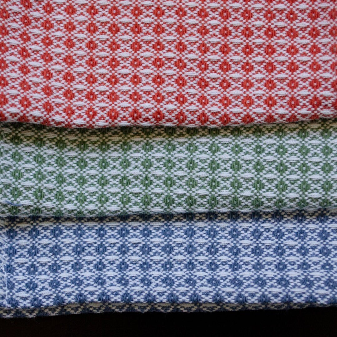 Hem And Tassel diamond waffle weave cotton cloths in red, green, and blue stacked for kitchen or bath use.