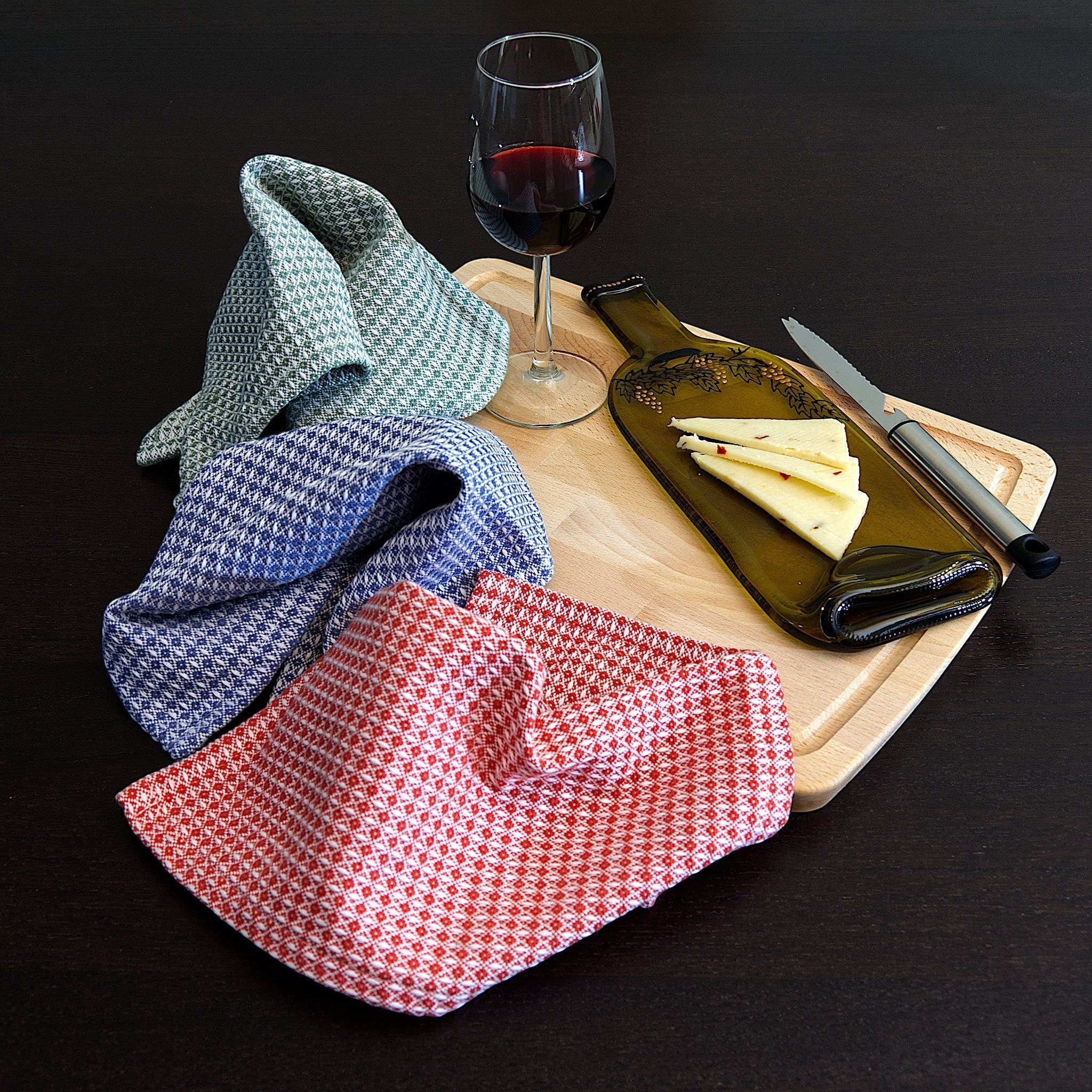 Hem And Tassel diamond waffle weave cotton cloths in red, blue, and green on a wooden board with cheese and wine.