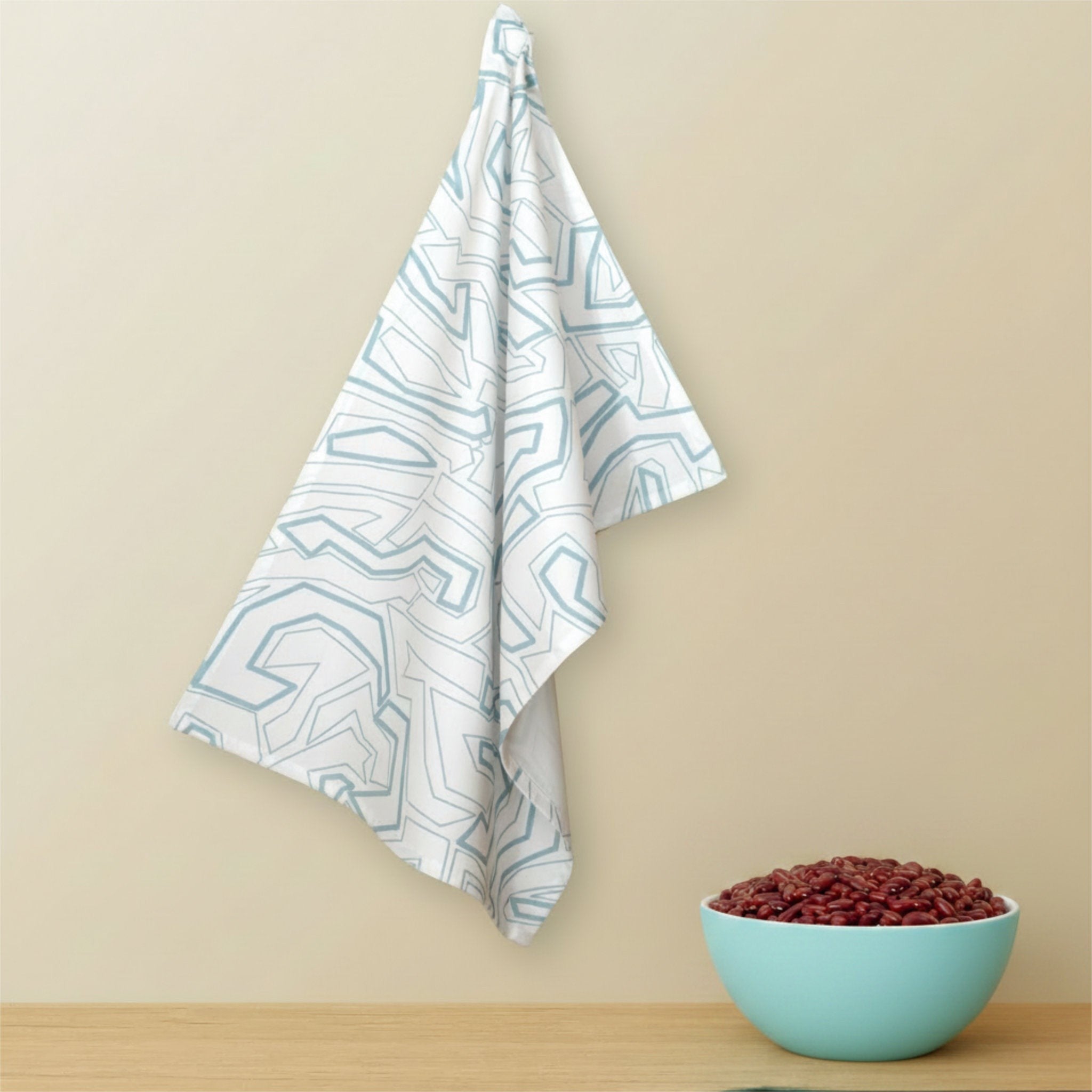 Hem And Tassel cotton kitchen towel with blue geometric squiggles pattern hanging on a neutral wall near a bean bowl