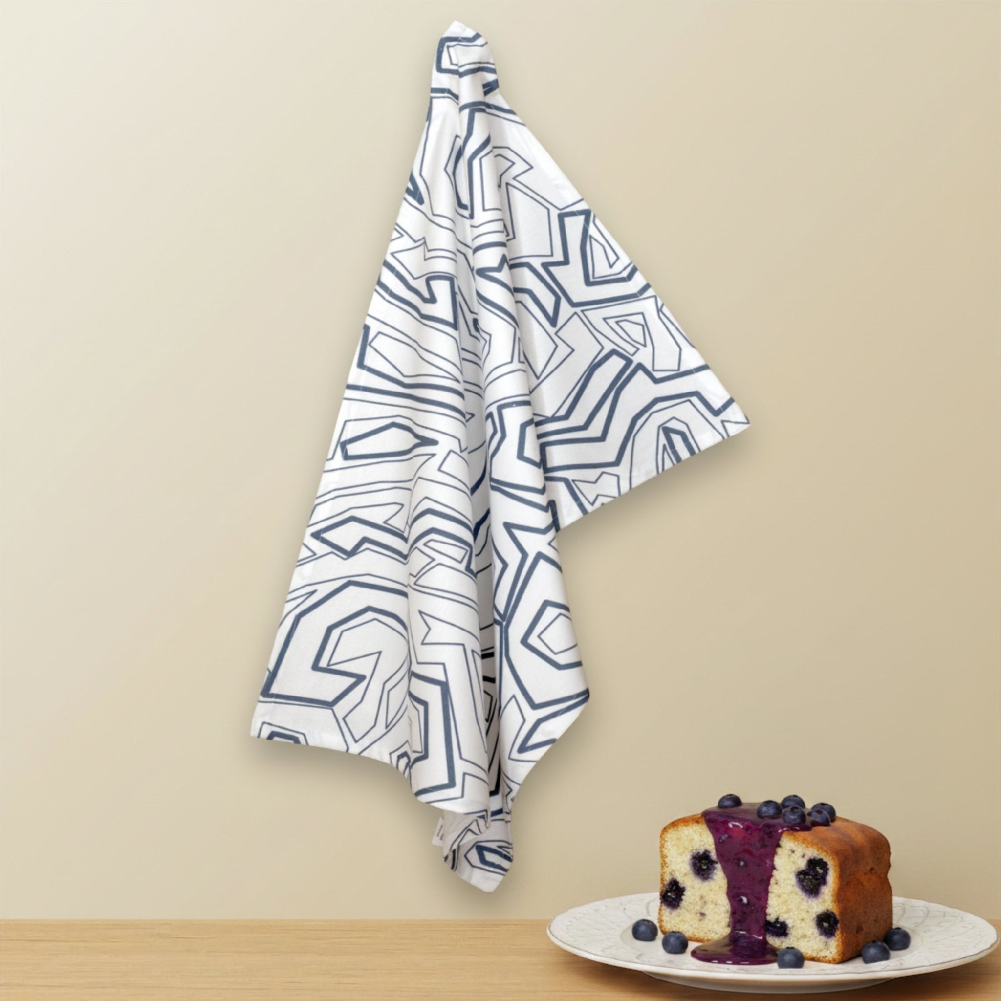Hem And Tassel Squiggles cotton kitchen towel with a modern geometric blue pattern hanging above a blueberry cake.