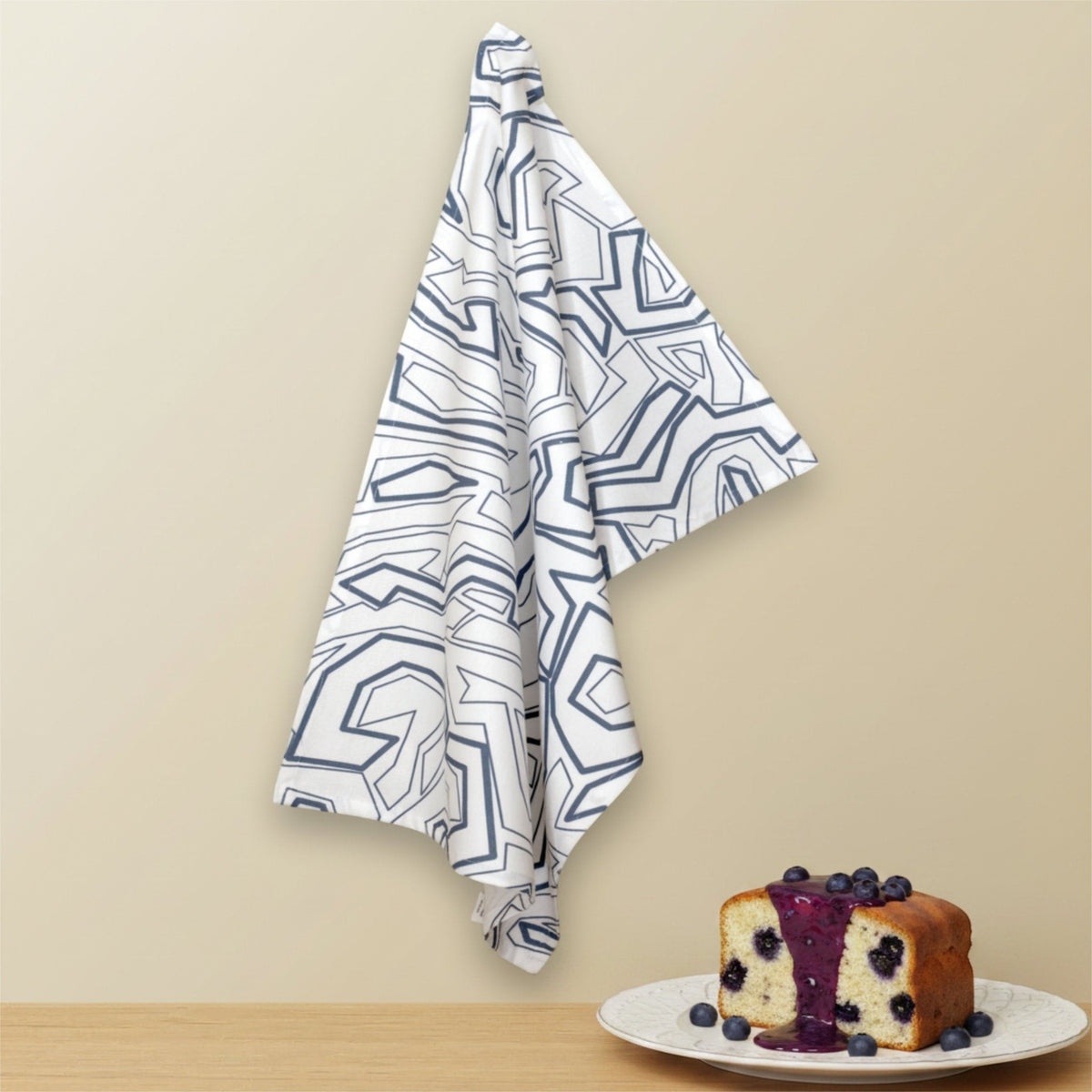 Hem And Tassel Squiggles cotton kitchen towel with a modern geometric blue pattern hanging above a blueberry cake.