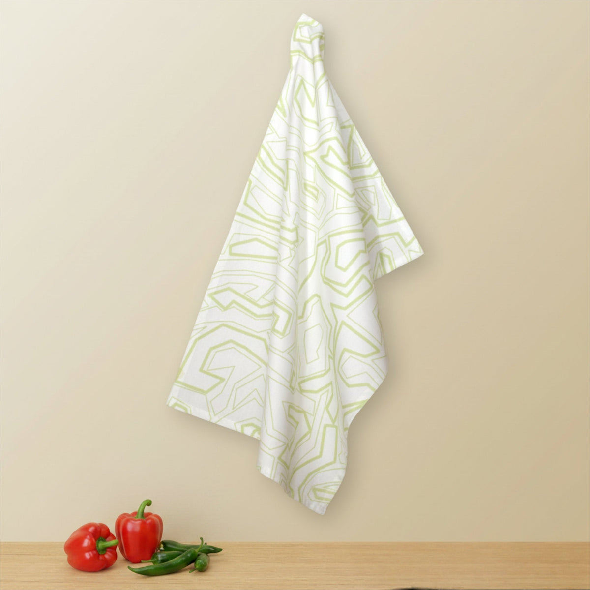 Hem And Tassel white cotton kitchen towel with light green geometric squiggles hanging against a beige wall