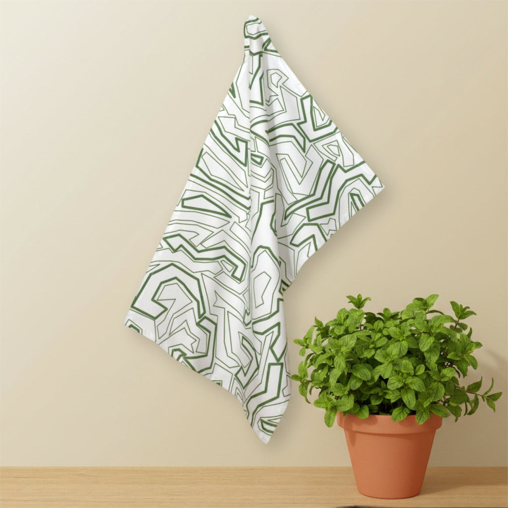 Hem And Tassel Squiggles cotton kitchen towel with green geometric pattern hanging on a wall near a potted plant.
