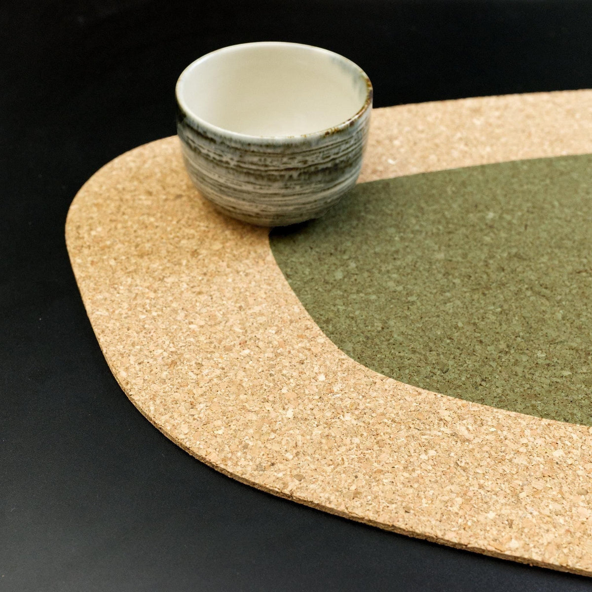 Hem And Tassel oversize kidney bean shaped natural cork placemat with a green accent and ceramic tea cup