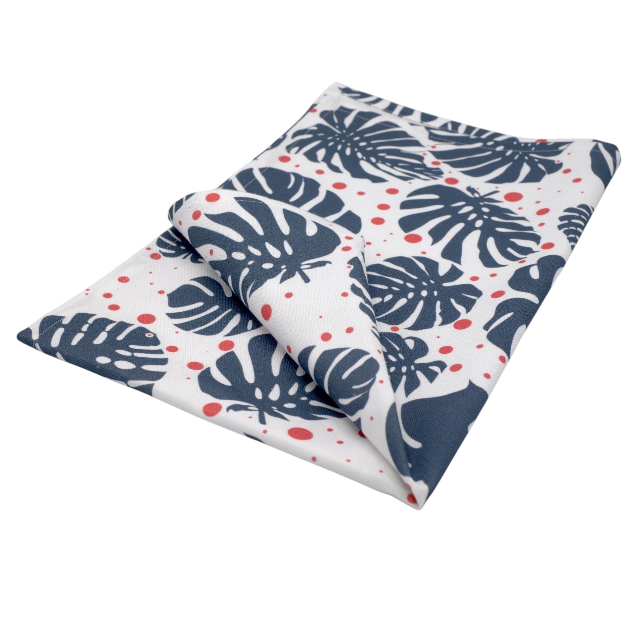 Hem And Tassel cotton kitchen towel featuring a white background with navy blue monstera leaves and red polka dots