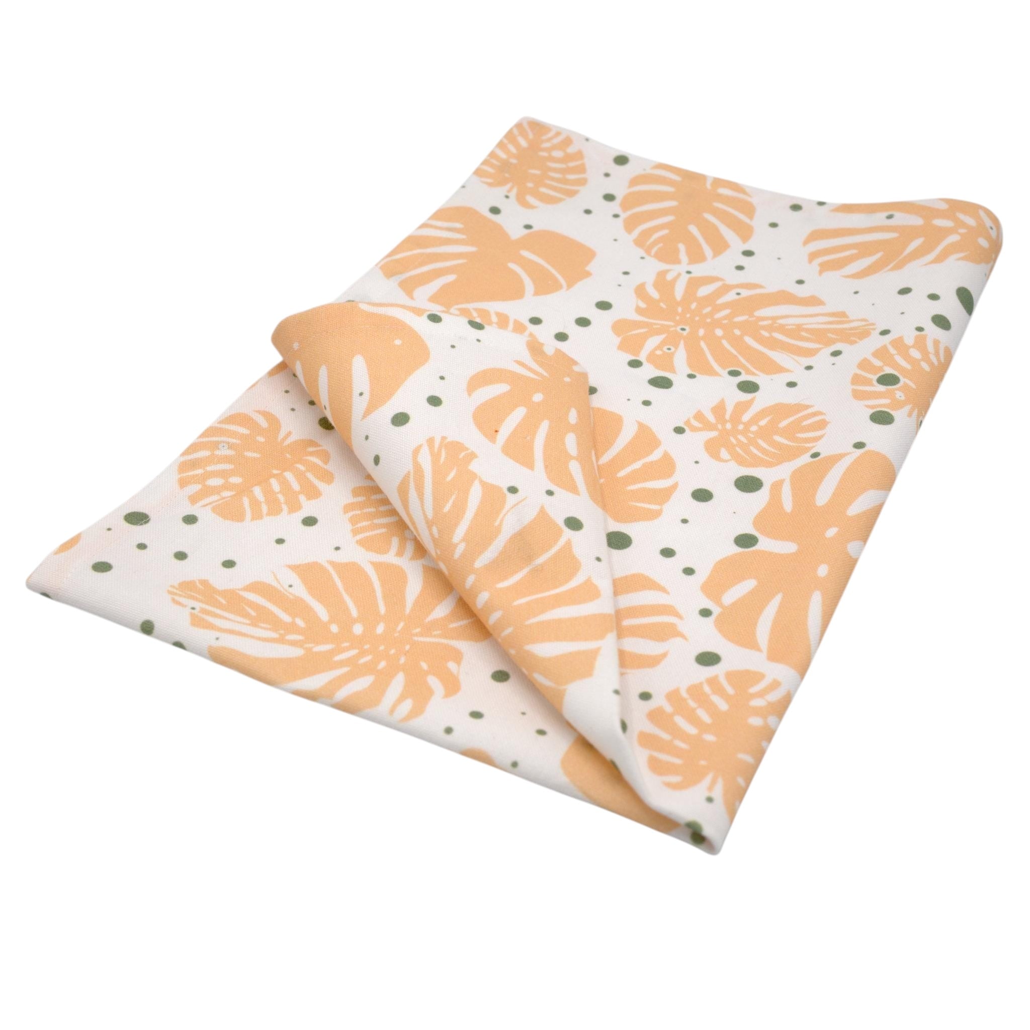 Hem And Tassel cotton kitchen towel featuring a peach and green monstera leaf print on a white background