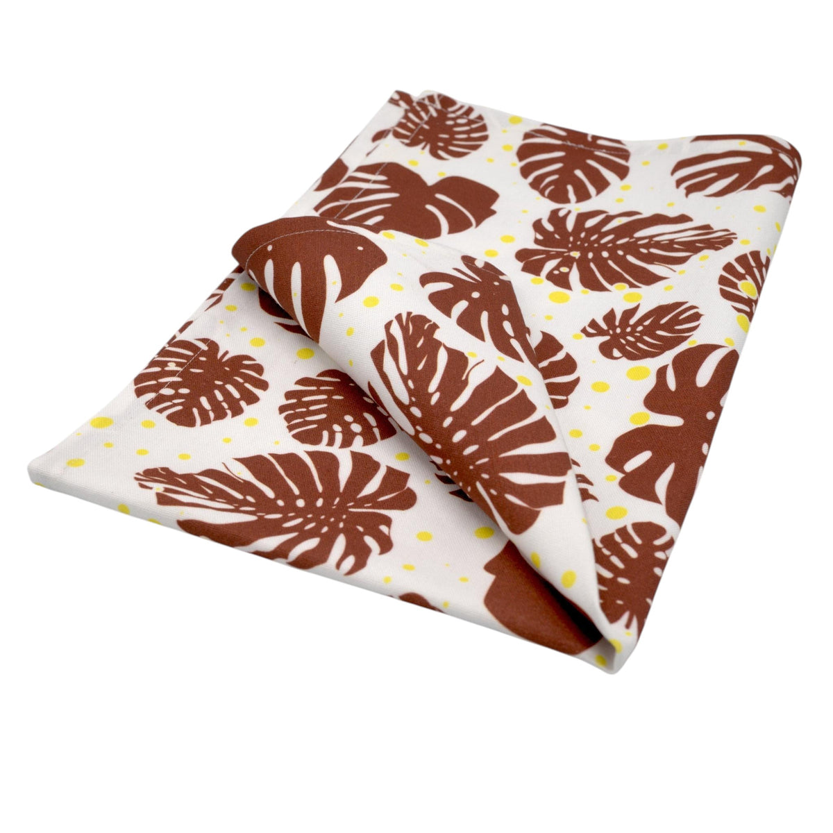 Hem And Tassel cotton kitchen towel featuring a brown monstera leaf pattern and yellow polka dots on white fabric.