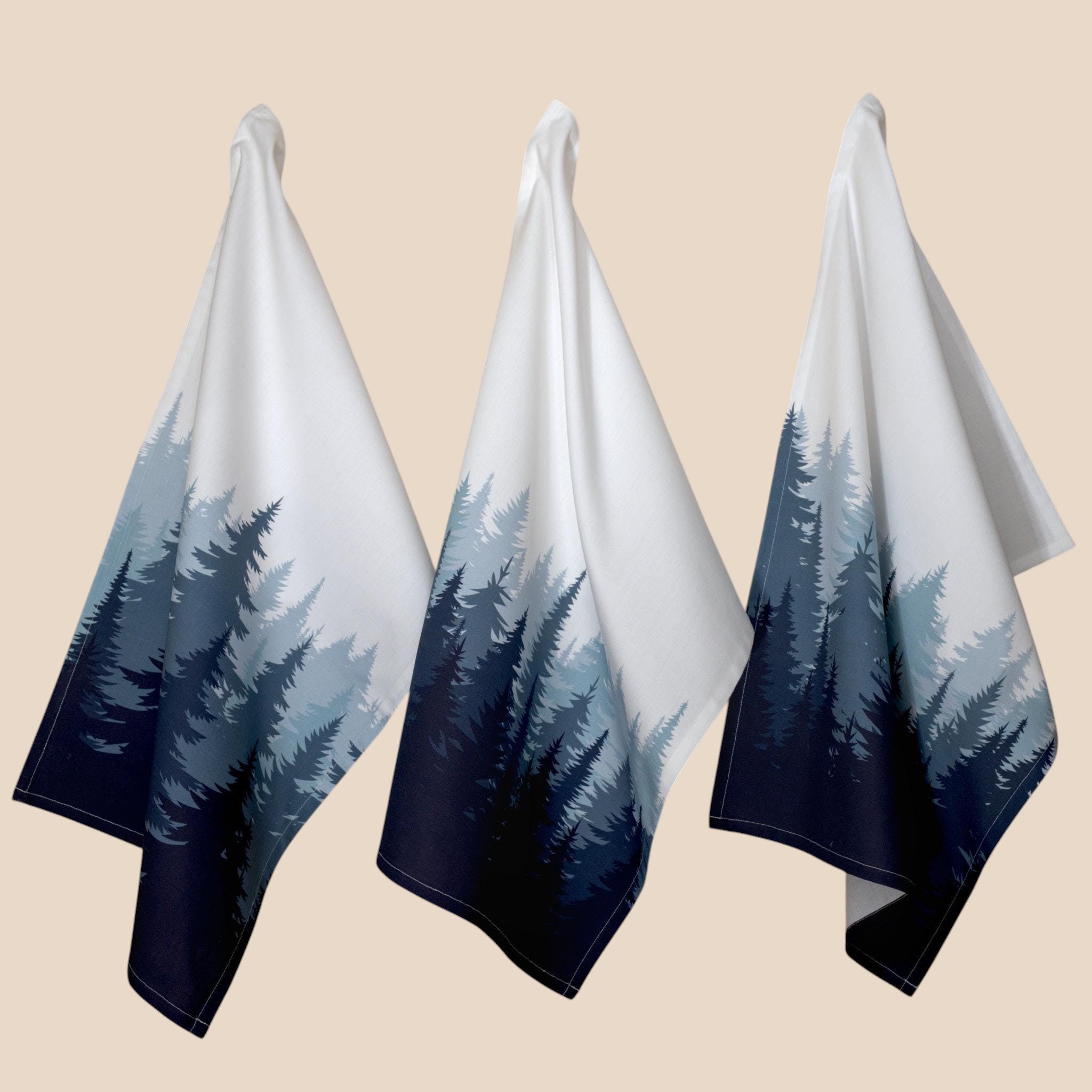 Hem And Tassel set of three cotton percale kitchen towels featuring an ombré pine forest print in shades of blue.