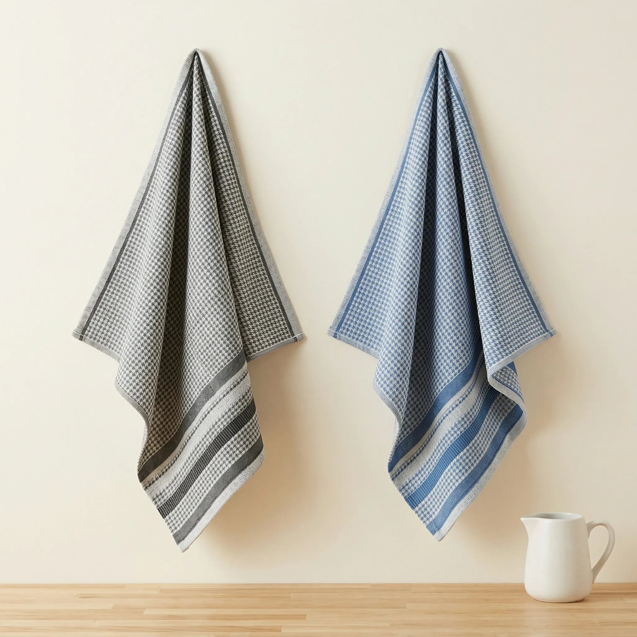 Jacquard kitchen towels of 100% cotton  with all-over houndstooth pattern - one in blue and one in black, hanging against a cream colored backdrop from Hem And Tassel 