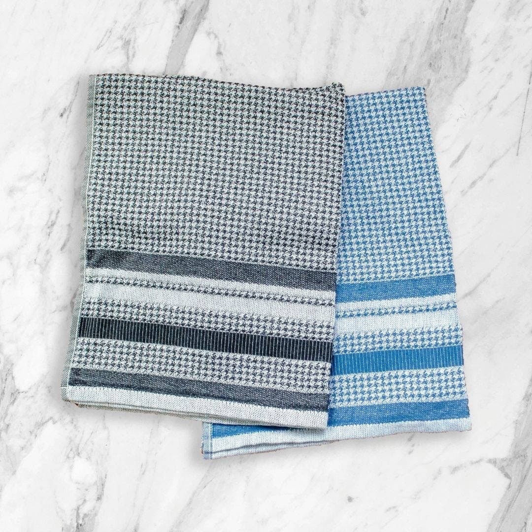 Two  houndstooth pattern towels, one black and white checkered and one blue and white striped, on a marble surface from Hem And Tassel 