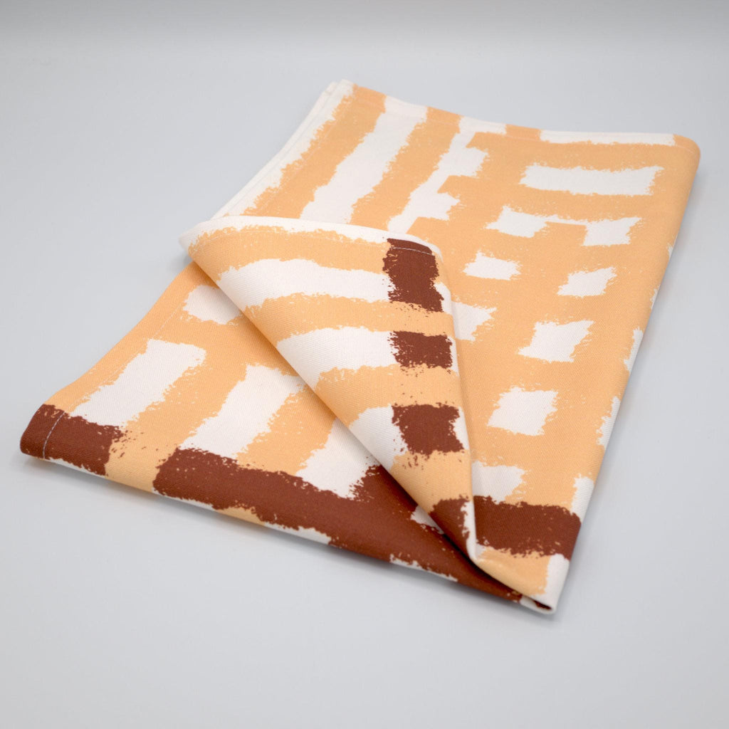 Folded cotton tea towel with buff and clay jute impossible pattern from Hem And Tassel on a gray background