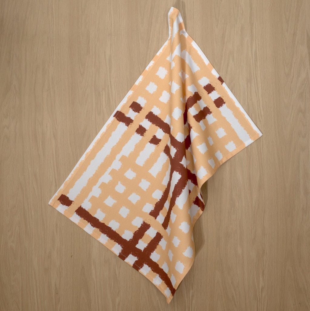 Hanging cotton tea towel with buff and clay jute impossible pattern from Hem And Tassel on a wood background
