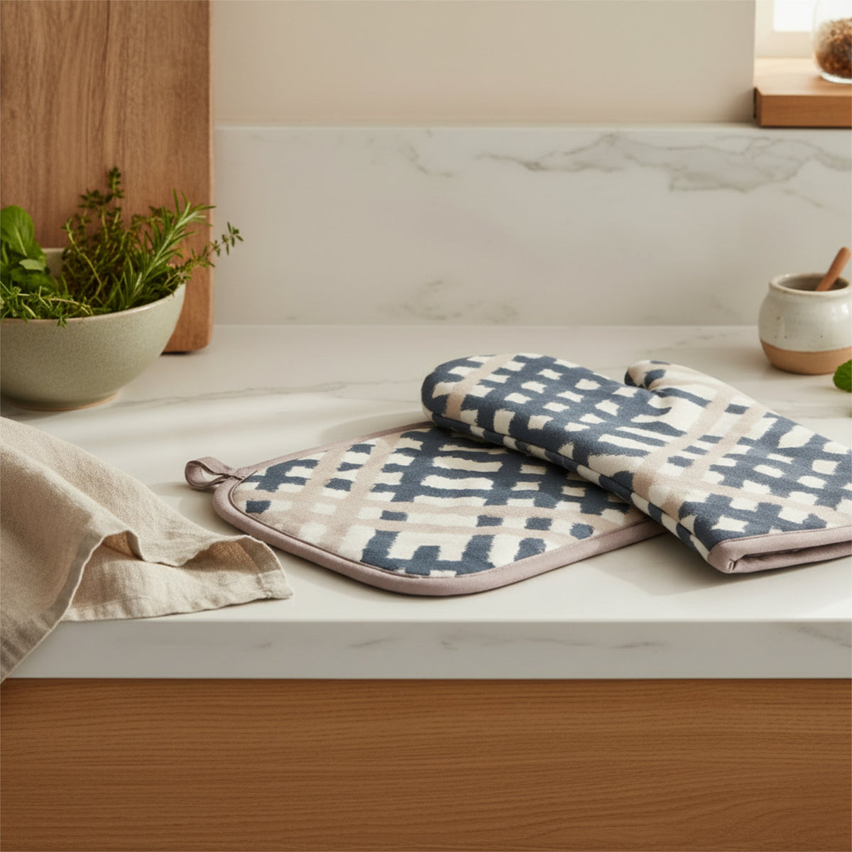 Checks patterned oven mitt and pot holder with a navy and cream geometric ikat design, resting on a white marble kitchen countertop next to a beige linen towel from Hem And Tassel 