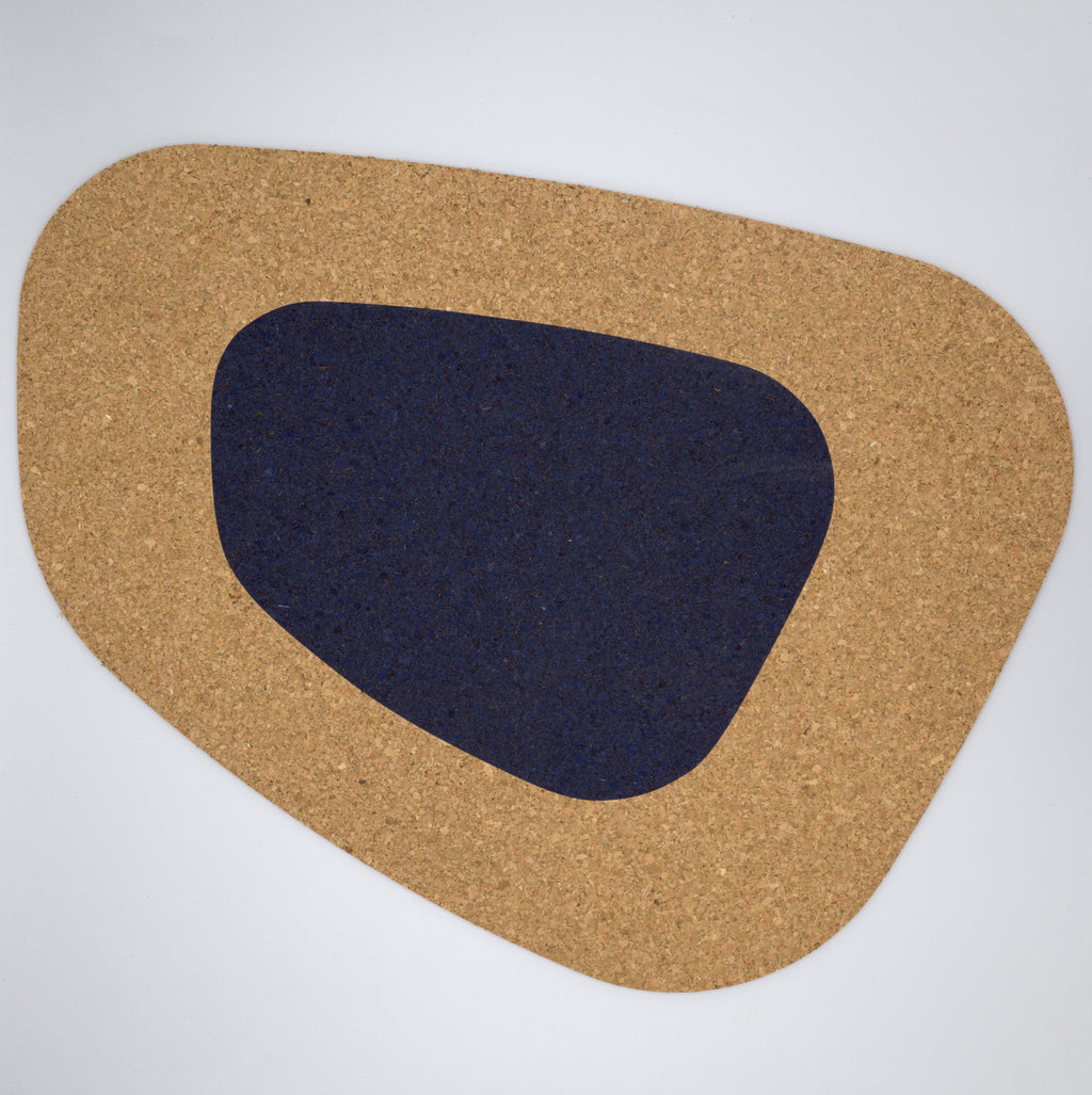 a kidney bean shaped large cork placemat with a navy color block on a white background