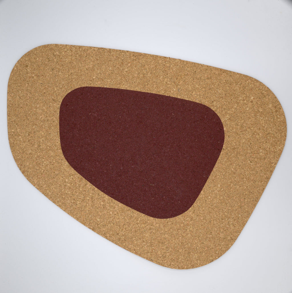 a kidney bean shaped large cork placemat with a clay color block on a white background