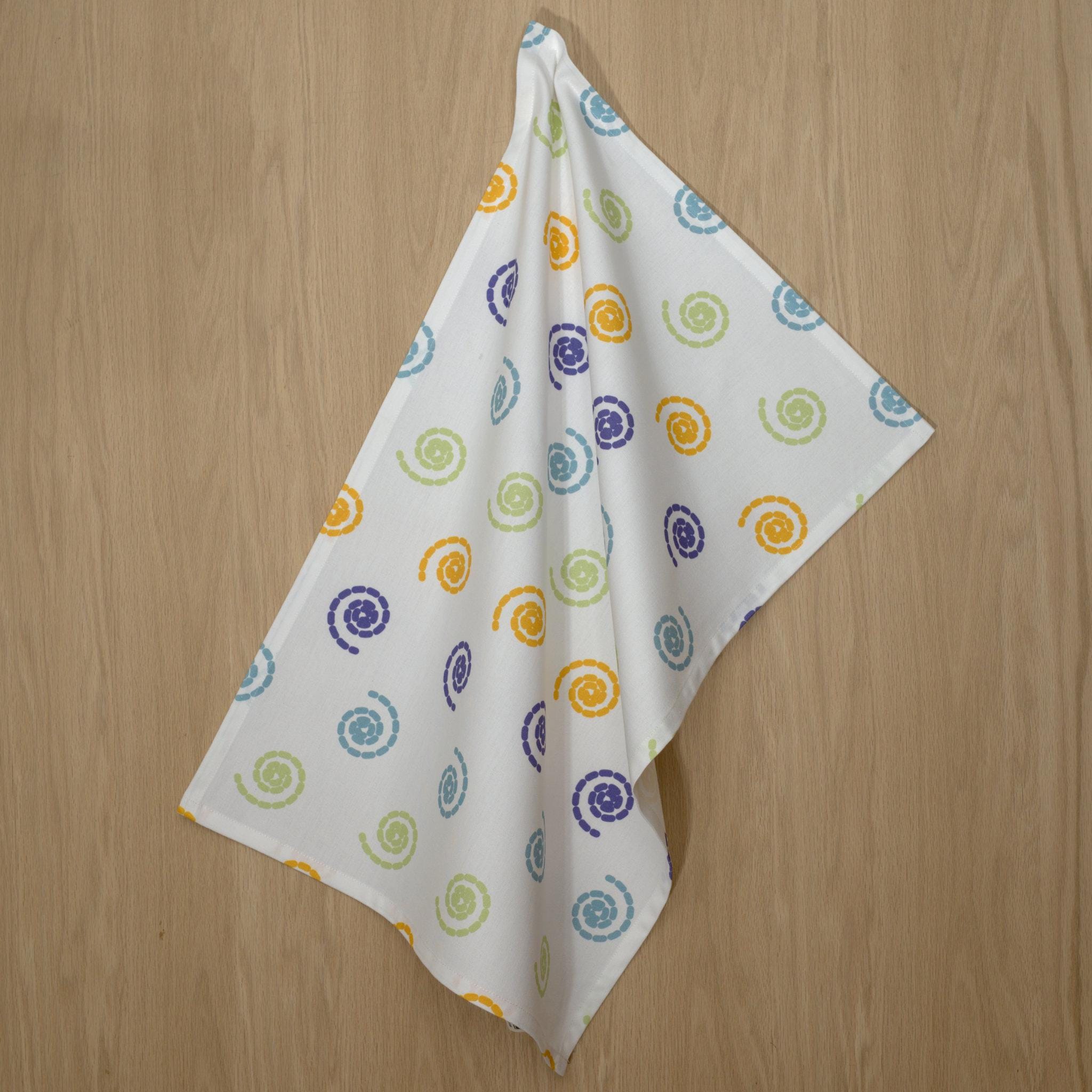 cotton percale tea towel in magic design from Hem And Tassel, with colorful swirls, hanging on a wood background