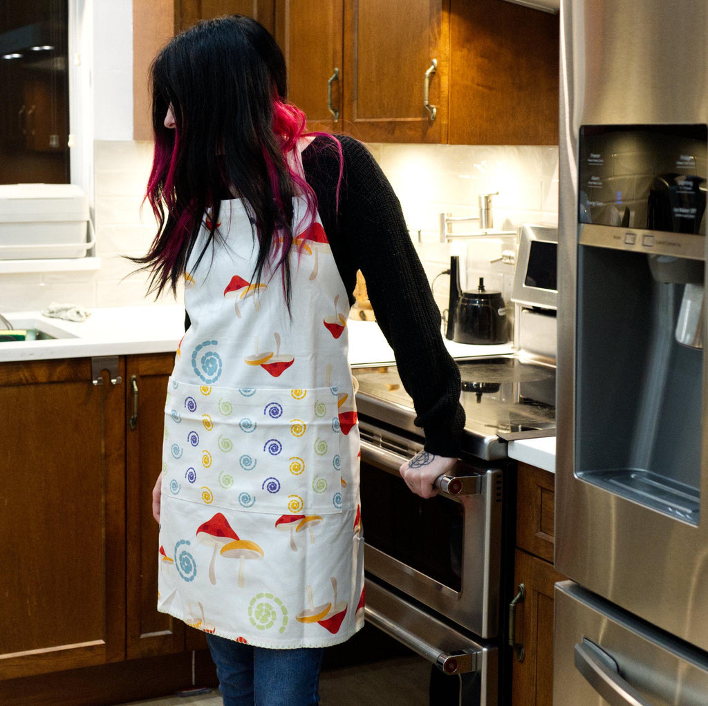 Person wearing a colorful magic mushroom apron in a kitchen from Hem And Tassel 