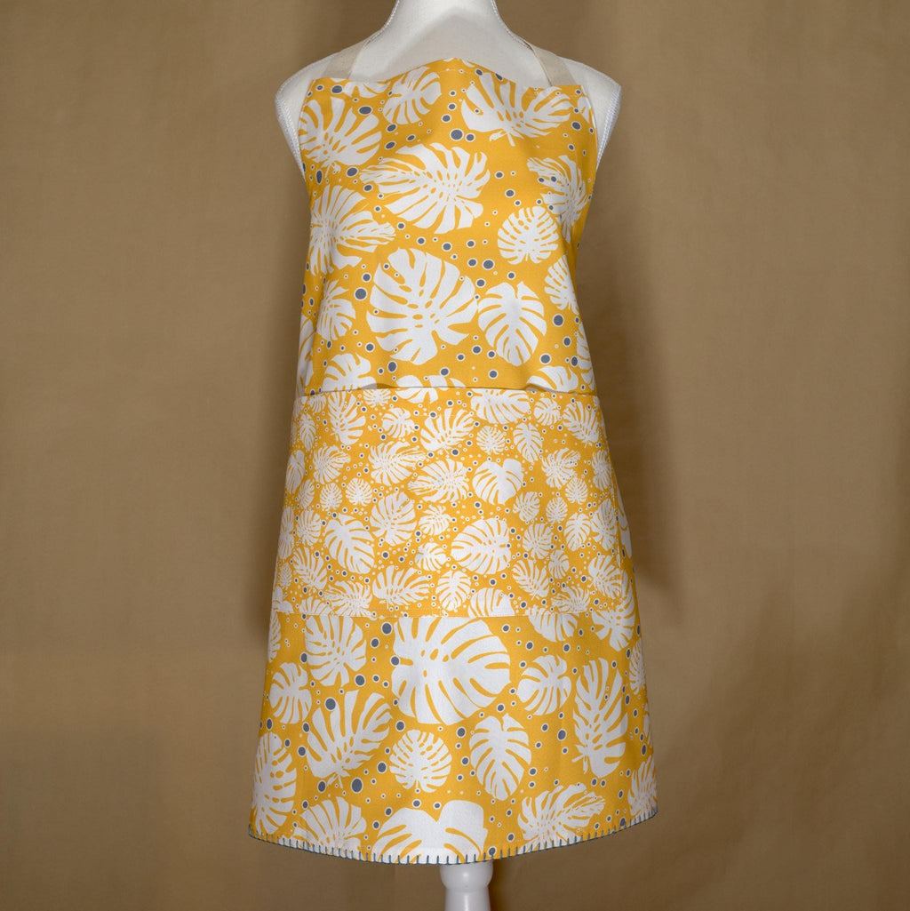 monster-ah apron orange with white monstera leaf pattern on a mannequin against a brown background from Hem And Tassel 