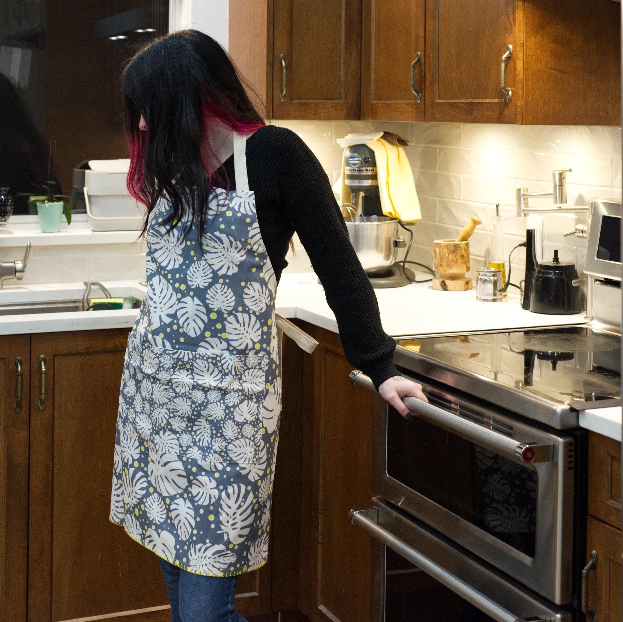Person wearing a monster-ah winter colored apron in a kitchen from Hem And Tassel 