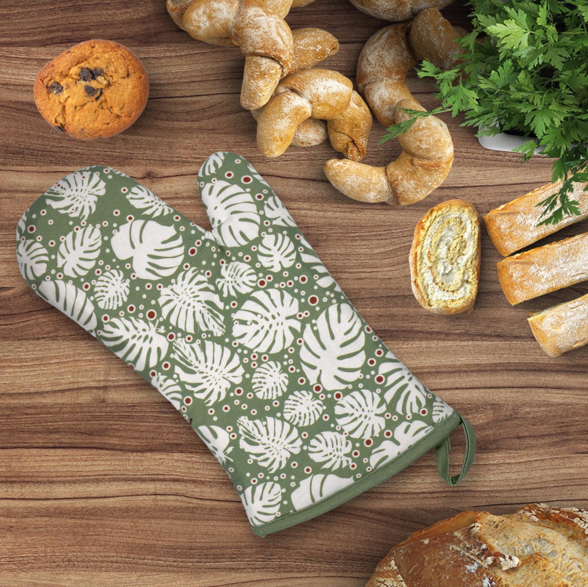 Green monster-ah oven mitt with white leaf pattern on a wooden table with baked goods from Hem And Tassel 