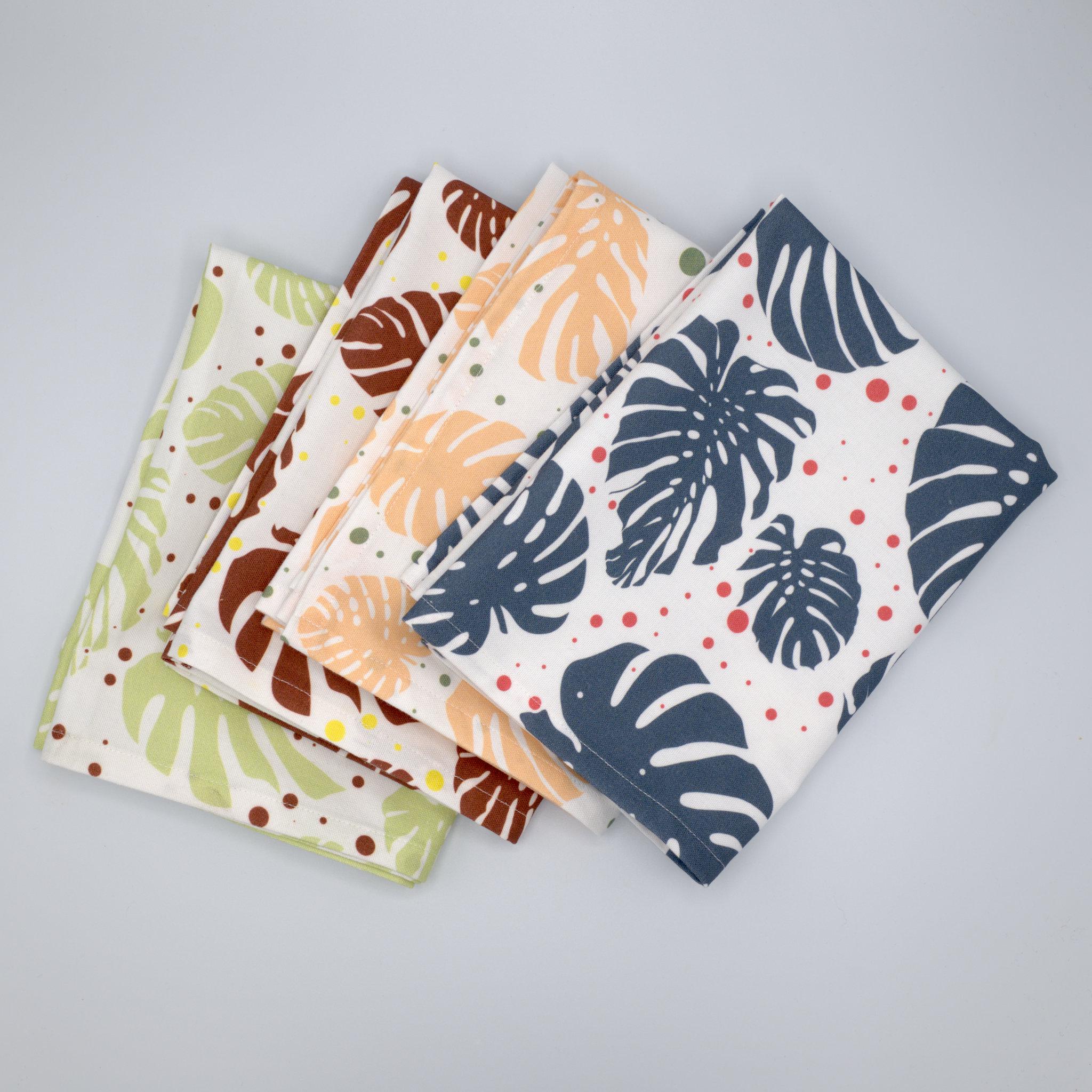 Set of monster ah kitchen towels in four colors fanned out with leaf patterns on a gray background from Hem And Tassel 