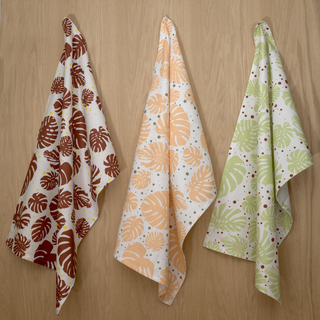 Three monster ah kitchen towels in colors hanging on a wooden surface from Hem And Tassel 