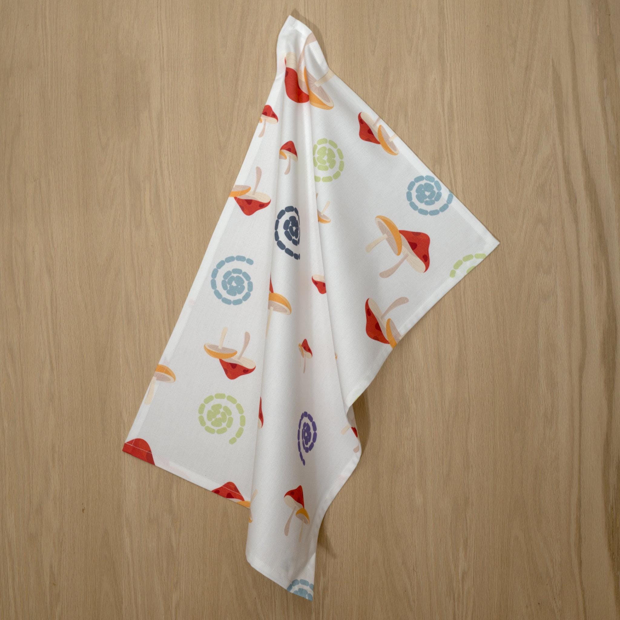 cotton percale tea towel in mushrooms design from Hem And Tassel, with colorful swirls, hanging on a wood background