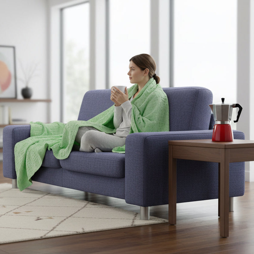pistachio wearable throw draped over a blue couch  and over a woman with a coffee cup in her hand on a carpeted floor of a living room