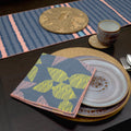 Table setting with a patterned napkin, plates, and coasters on arough stripes table runner with color accent from Hem And Tassel 