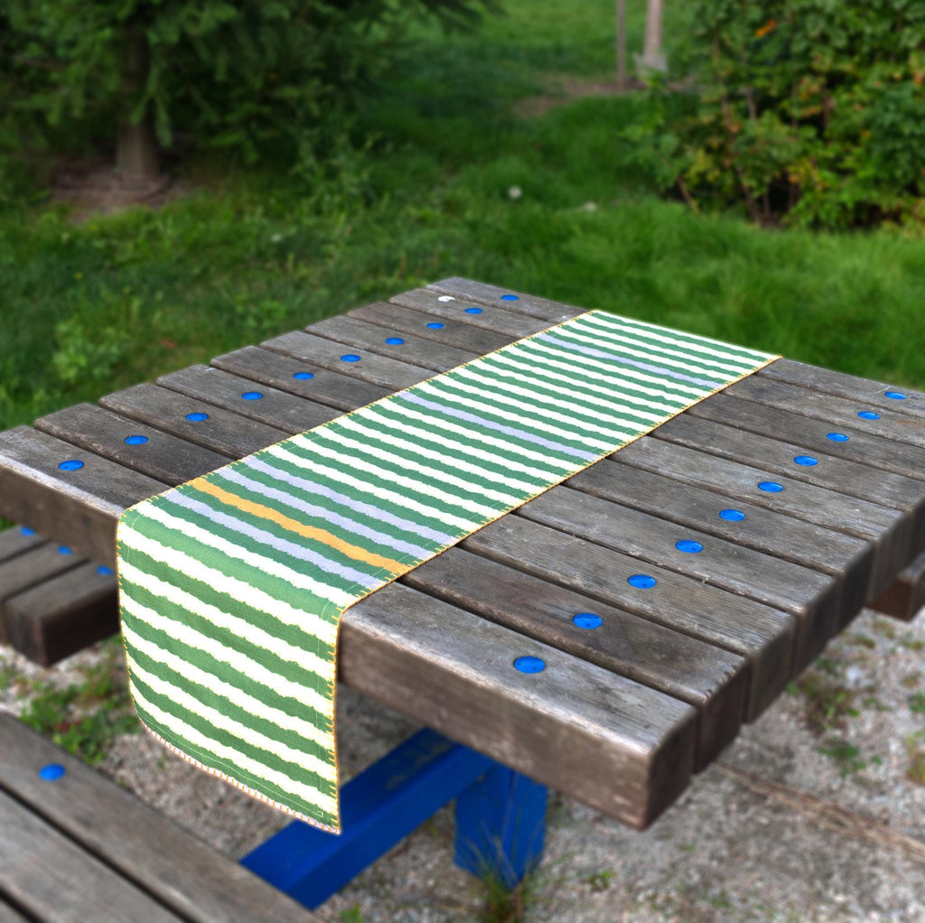 Green rough stripes table runner with color accent on a wooden picnic table outdoors from Hem And Tassel 