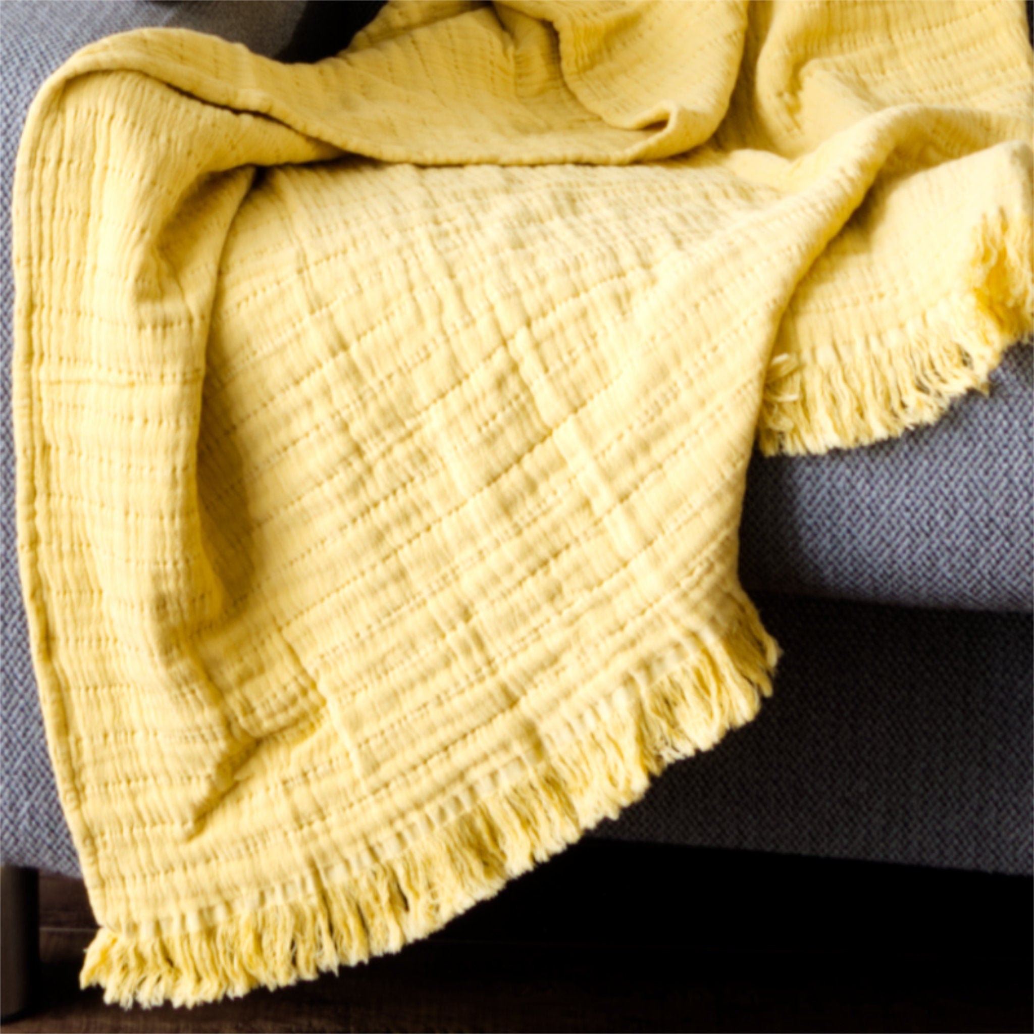 Yellow textured seersucker wearable throw draped over a gray sofa from Hem And Tassel 