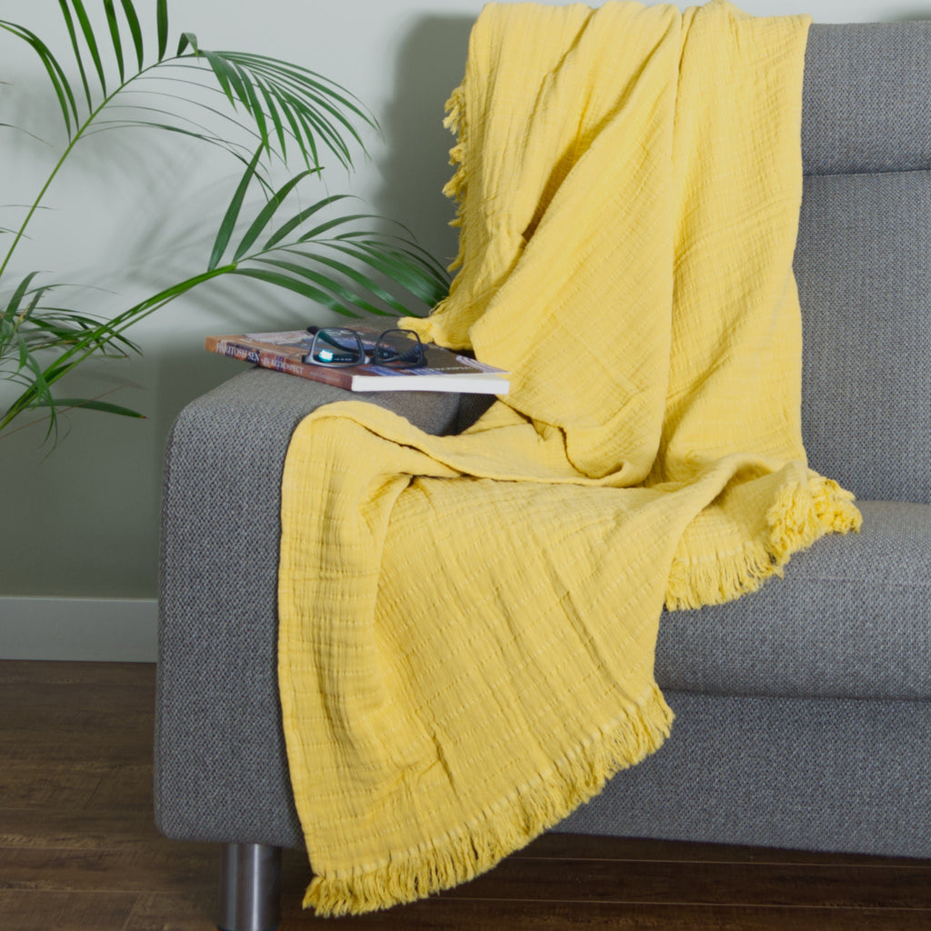 Ochre seersucker wearable throw draped over a gray sofa with a plant in the background from Hem And Tassel 