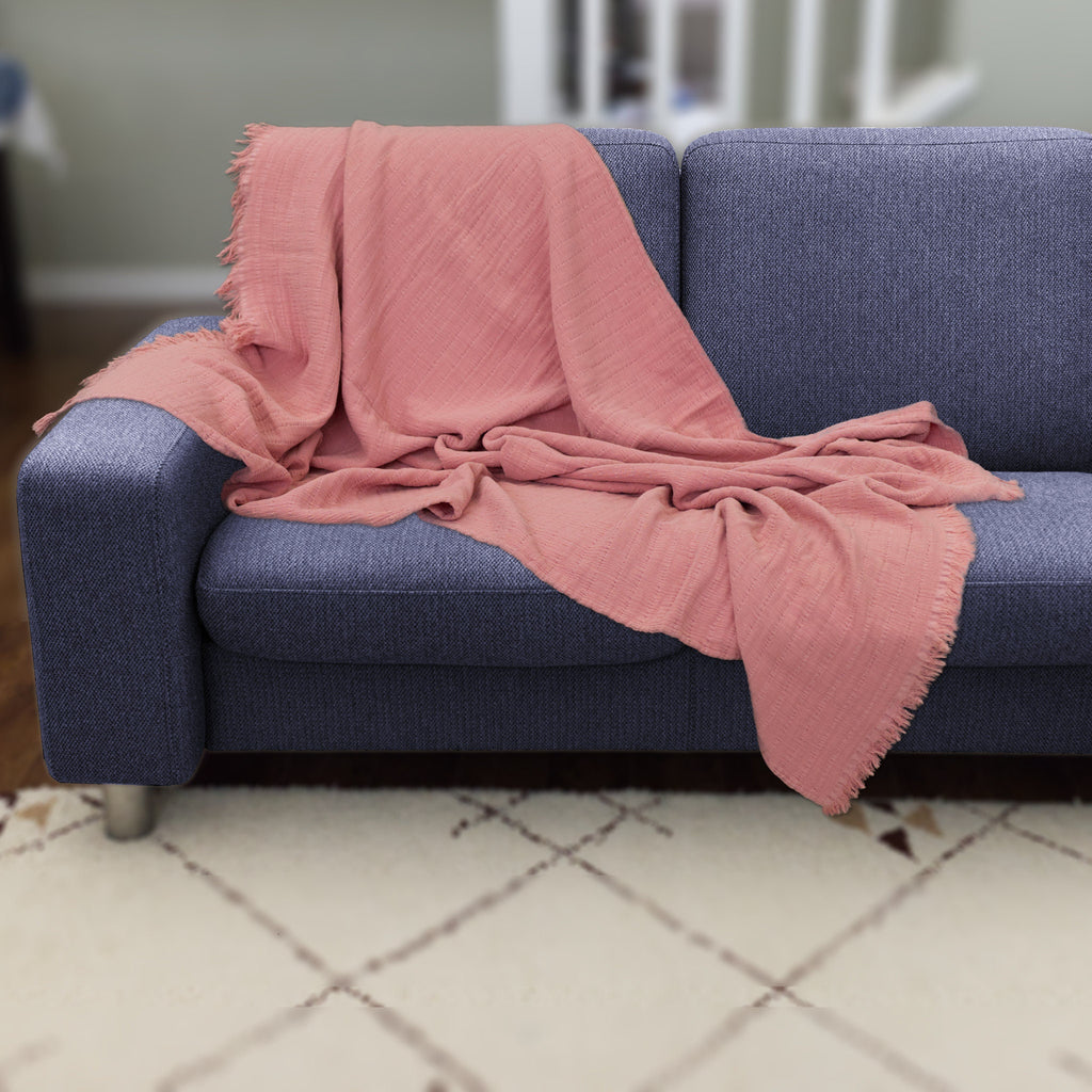 Blue sofa with a pink seersucker wearable throw draped over it in a room setting from Hem And Tassel 