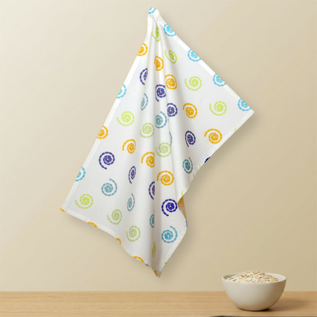 A white kitchen towel with a colorful spiral pattern hangs from a hook on a beige wall above a wooden surface with a small bowl of oats from Hem And Tassel