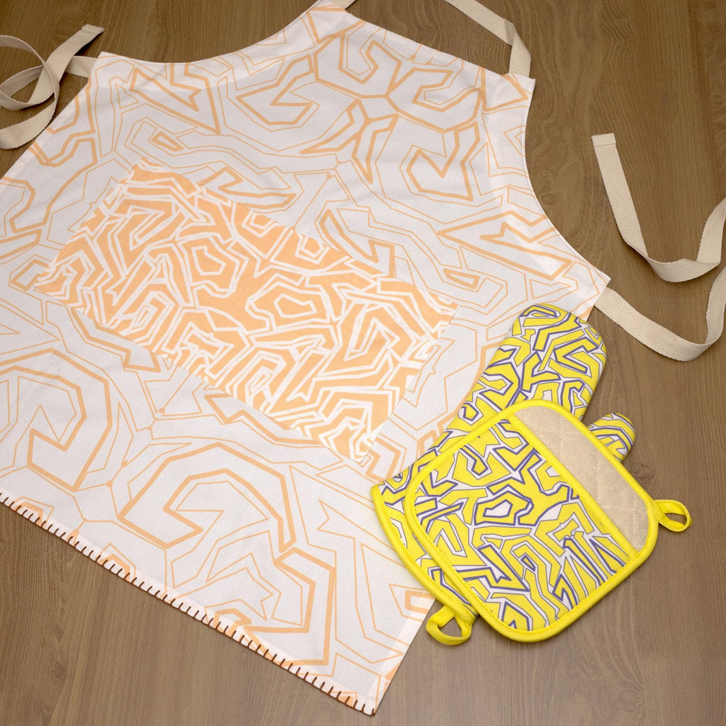 Patterned squiggles apron and yellow oven mitt on a wooden surface from Hem And Tassel 