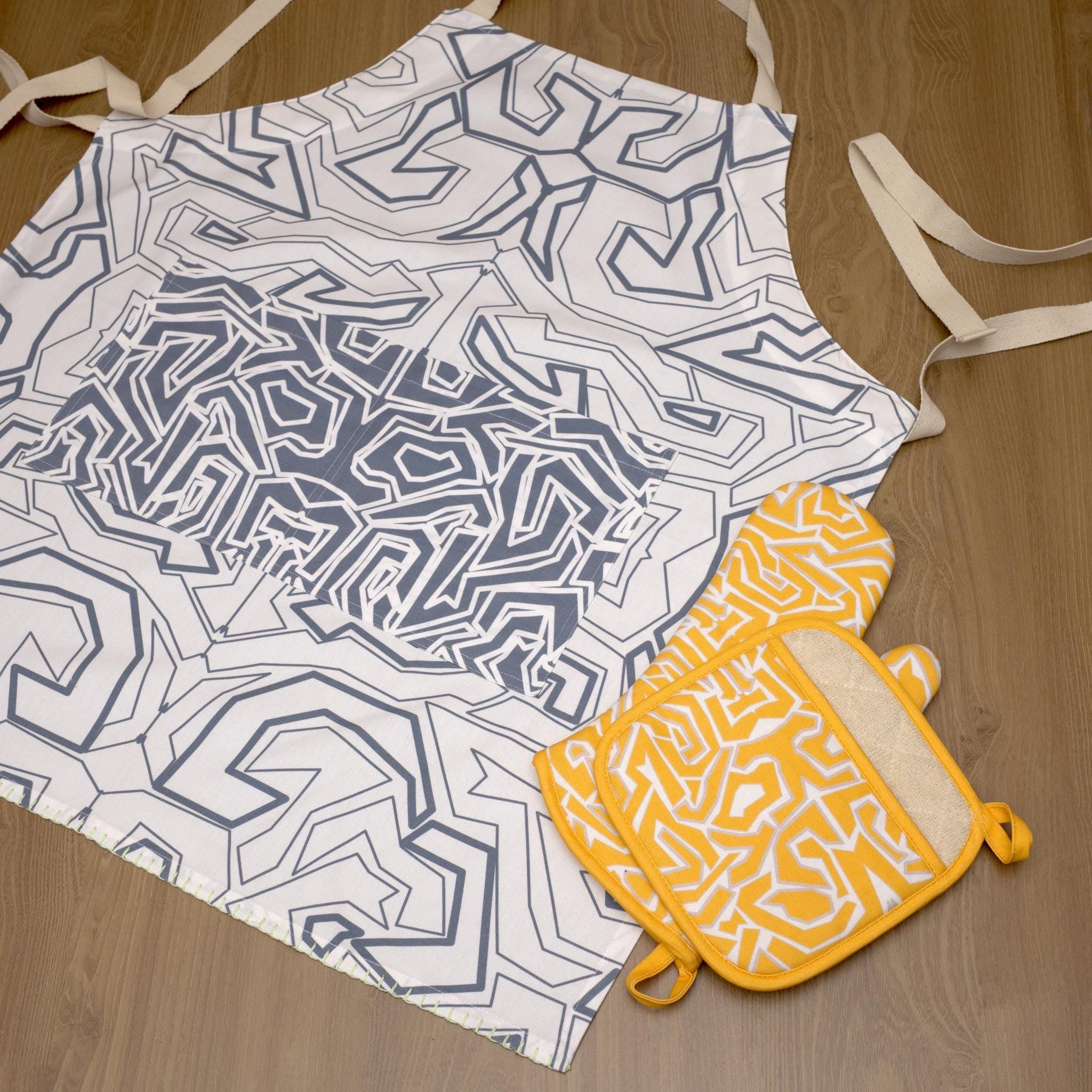 Geometric-patterned squiggles apron and matching oven mitt on a wooden surface from Hem And Tassel 