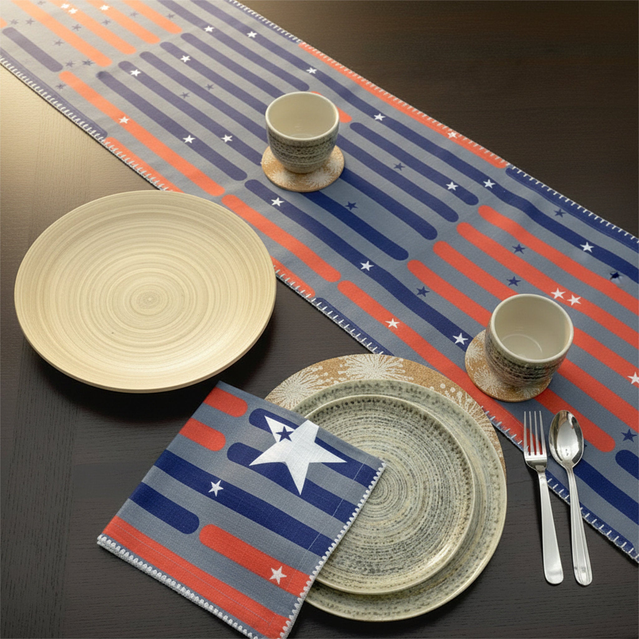 A styled table setting featuring a patriotic-themed table runner, matching napkin, and ceramic plates and cups on a dark wooden table from Hem And Tassel 