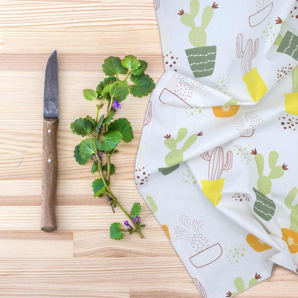 thorny issue kitchen towel with cactus pattern on a wooden surface with a knife and herbs from Hem And Tassel 