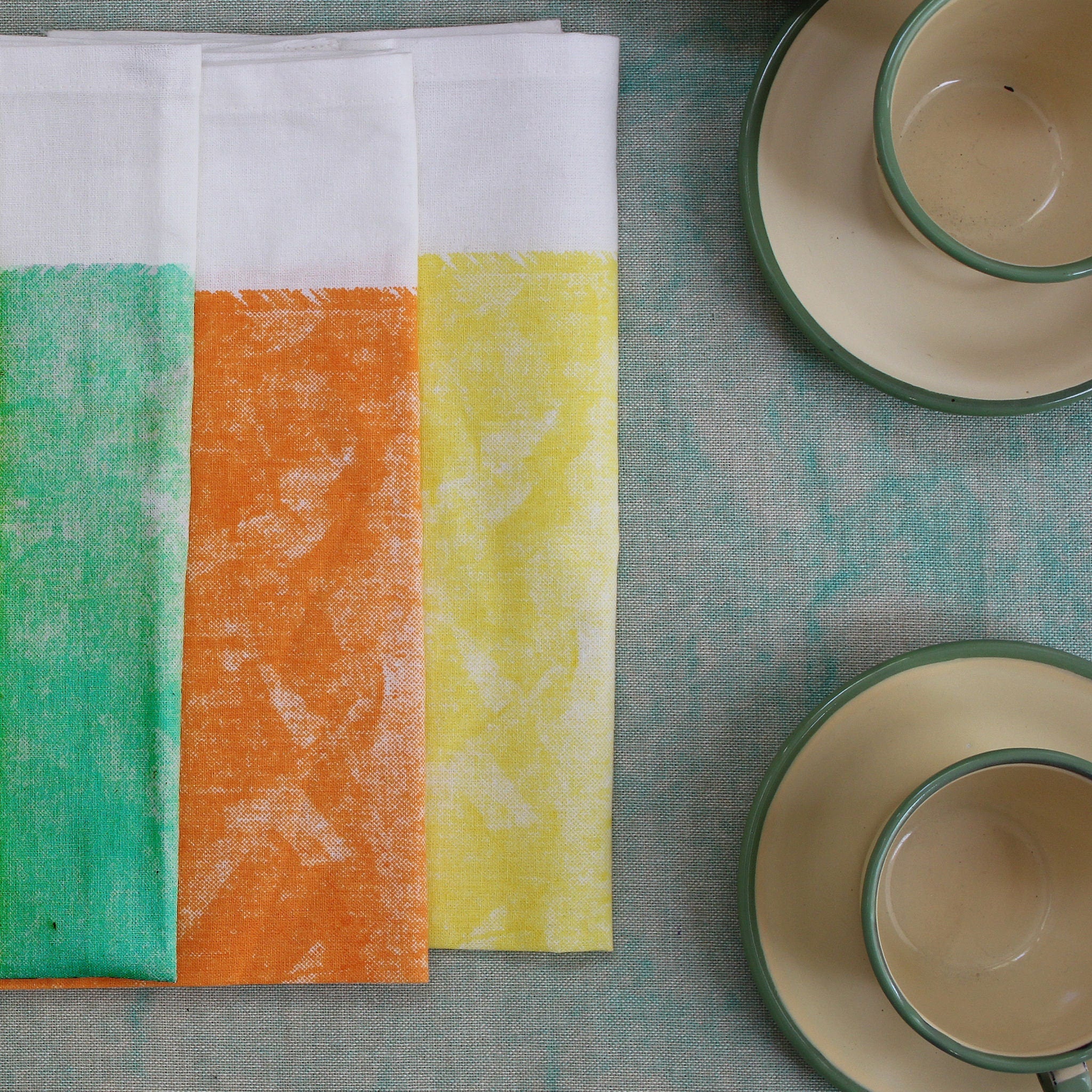 Colorful towels in rich cotton, in tie-dye retro style, from Hem And Tassel, folded on table with 2 sets of cups and saucers
