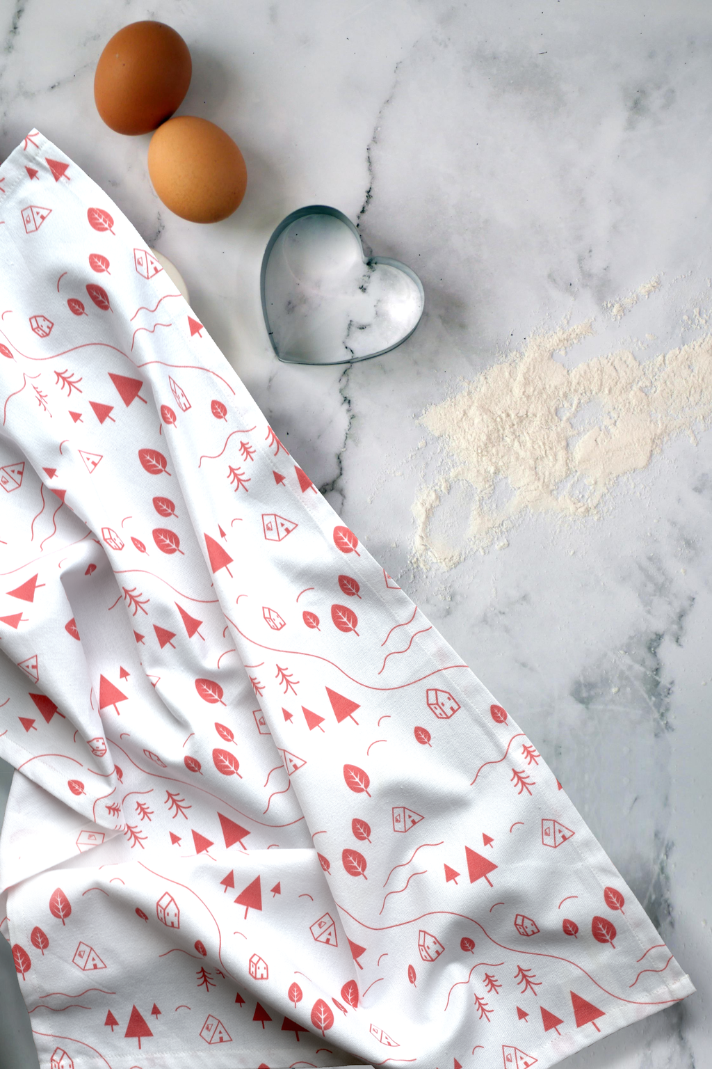 White tiny countryside kitchen towel with pink patterns on a marble surface with eggs and a heart-shaped cookie cutter from Hem And Tassel 